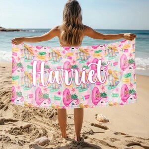 May include: A pink beach towel with a flamingo and pineapple pattern. The towel has the name "Harriet" printed in white on it.