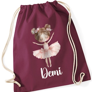 May include: Burgundy drawstring bag with a white personalised name "Demi" and a graphic of a ballerina girl with pink tutu and brown hair.