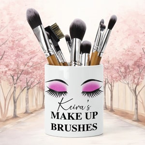Puede incluir: Portacepillos de maquillaje de cerámica blanca con un diseño de ojo rosa y negro y el texto "Keira's Make Up Brushes".