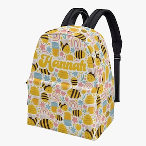 May include: A yellow and white backpack with a bee and honeycomb pattern. The backpack has a black zipper and adjustable straps. The name "Hannah" is printed in yellow on the front of the backpack.