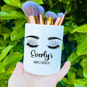 Könnte beinhalten: Weißer Keramik-Make-up-Pinselhalter mit einem Glitzer-Augen-Design und dem Text "Everly's Brushes".