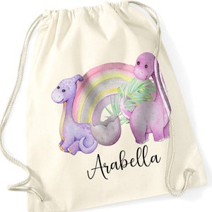 May include: A white drawstring bag featuring a purple dinosaur and a rainbow design. The bag is personalised with the name "Arabella".