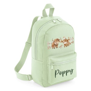 May include: A light green canvas backpack featuring a brown highland cow design and the name "Poppy" embroidered on the front.