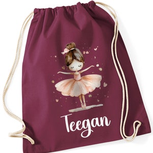 Pode incluir: Saco de cordão bordô com uma ilustração de bailarina rosa e o nome "Teegan" impresso em branco.