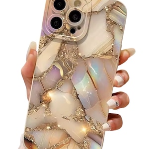 以下が含まれることがあります： 大理石模様の携帯電話ケース。白、ベージュ、金色の色が混ざり合い、虹色のアクセントがあります。カメラ部分は薄紫色の縁取り。ケースは人が持っています。