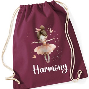 May include: Burgundy drawstring bag with a white personalised name "Harmony" and a graphic of a ballerina with a pink tutu and brown hair.