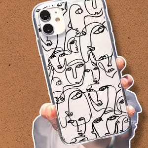 Puede incluir: Funda de teléfono transparente con fondo blanco y diseño de arte lineal negro de rostros abstractos. La funda tiene un borde transparente y está sujeta con una mano.
