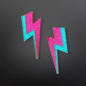 Puede incluir: Un par de pendientes de rayo de color rosa y azul con purpurina. Los pendientes están hechos de un material brillante y tienen un diseño audaz y geométrico.