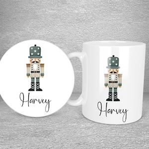 Puede incluir: Taza y posavasos de cerámica blanca con una ilustración gris y blanca de un cascanueces. La taza y el posavasos están personalizados con el nombre "Harvey".