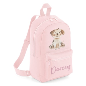 Puede incluir: Mochila de lona rosa con una ilustración de perro de dibujos animados y el nombre "Darcey" impreso en el bolsillo delantero.