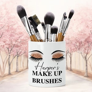 Könnte beinhalten: Weißer Keramik-Make-up-Pinselhalter mit einem goldenen Glitzer-Augen-Design und dem Text "Harper's Make Up Brushes".