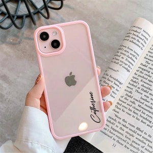 May include: A pink clear phone case with a raised black border. The case has a cutout for the camera lens and a clear back. The name "Catherine" is written in black on the back of the case.