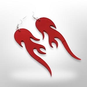 Puede incluir: Un par de pendientes de acrílico rojo con forma de llamas. Los pendientes son de estilo colgante y tienen un gancho plateado.