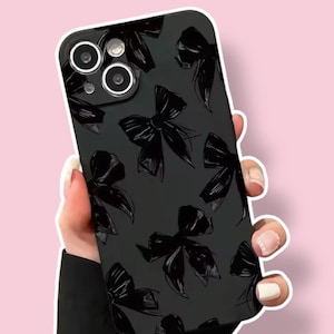 May include: Black phone case featuring a repeating pattern of black bow illustrations. The case has a glossy finish and a camera cutout. The design is set against a soft pink background.