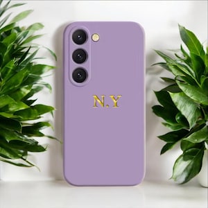 May include: A lavender phone case with a gold N.Y. monogram. The case has a raised camera bump with three lenses.