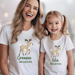 May include: Two white t-shirts with a cartoon reindeer and the text "Grannie Believes" and "Isla Believes". A woman and a young girl are wearing the shirts.