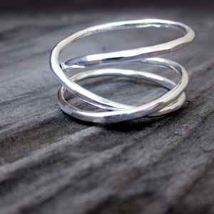 May include: A silver ring with a unique, twisted design. The ring is made of three bands of silver that are intertwined and hammered for a textured look.