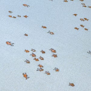 Pode incluir: Um tecido azul-claro com um padr&atilde;o repetitivo de pequenas ilustra&ccedil;&otilde;es de peixes dourados espalhadas pela superf&iacute;cie. O t&ecirc;xtil tem uma textura tecida vis&iacute;vel e os peixes est&atilde;o representados em v&aacute;rias orienta&ccedil;&otilde;es, criando um design simples e uniforme.