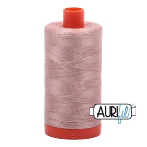 May include: A spool of pale pink thread with a red plastic bobbin and the Aurifil logo in blue.
