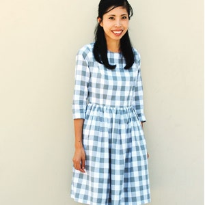 May include: A woman wearing a gray and white gingham dress with 3/4 sleeves. The dress has a fitted bodice and a full skirt.