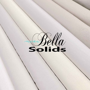 May include: Close-up of several rolls of white fabric with the text "moda Bella Solids™" printed on the fabric.