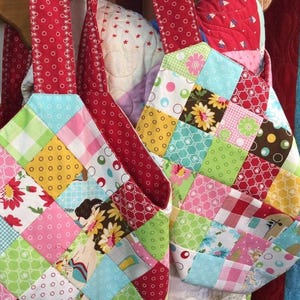 May include: Two patchwork fabric bags with red handles. The bags are made of colorful squares of fabric with different patterns, including floral, polka dot, and plaid.
