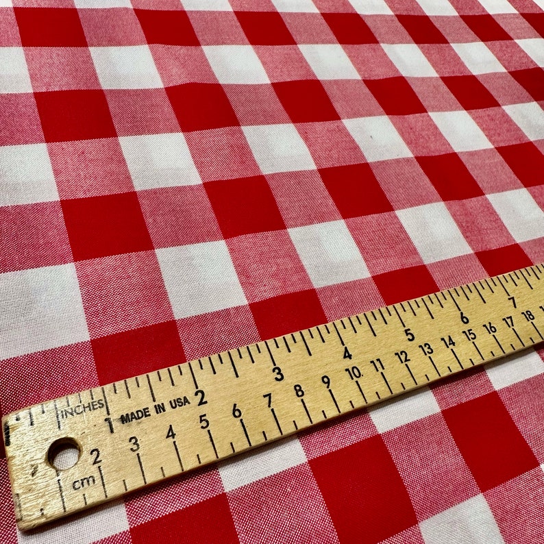 May include: Red and white checkered fabric with a wooden ruler measuring 18 inches. The ruler is marked in inches and centimeters.