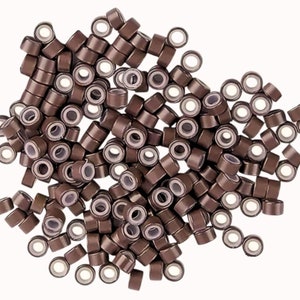 Könnte beinhalten: Ein großer Haufen brauner Mikroringen für Haarverlängerungen. Die Ringe sind aus strapazierfähigem Kunststoff und haben ein kleines Loch in der Mitte.