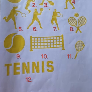 May include: A sheet of gold-colored tennis-themed decals. The sheet includes illustrations of tennis players, tennis balls, crossed tennis rackets, a tennis net, and the word "TENNIS".