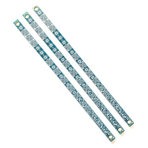 Peut inclure: Trois lanières en tissu bleu sarcelle avec un motif géométrique blanc. Chaque lanière a un œillet métallique à chaque extrémité.