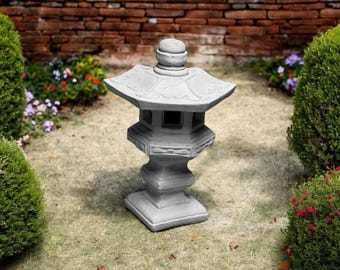 May include: A gray stone Japanese lantern with a traditional design. The lantern is sitting on a bed of brown grass.