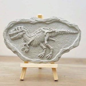 May include: A grey dinosaur skeleton fossil replica on a small wooden easel. The fossil is set in a grey rock-like material.
