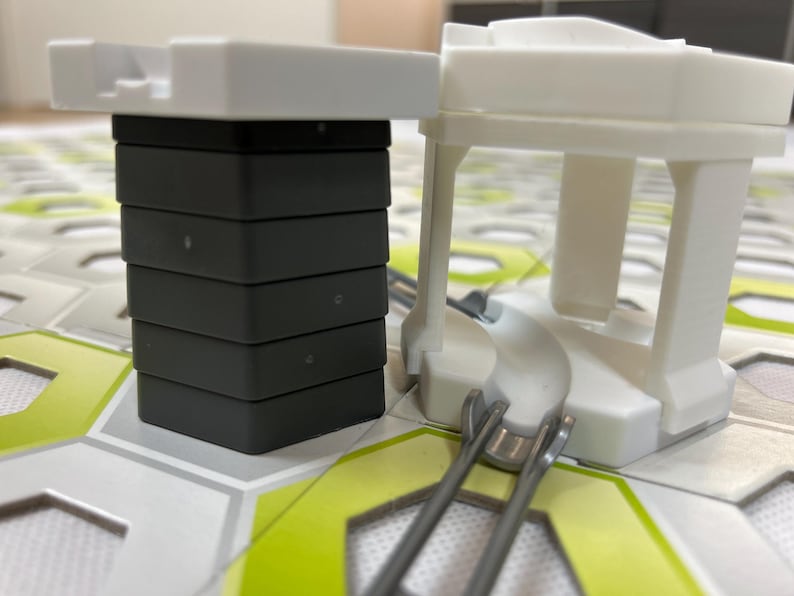 Puede incluir: Primer plano de un juego de construcci&oacute;n. El conjunto incluye una pila de bloques grises oscuros rematados con una pieza blanca, y una estructura blanca con una base curva y ra&iacute;les met&aacute;licos. La base est&aacute; sobre una superficie estampada.