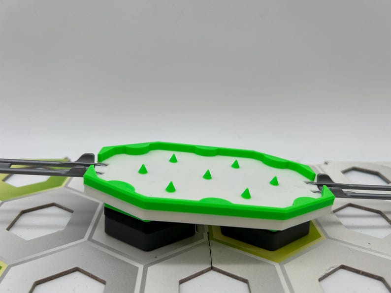 Pode incluir: Uma pe&ccedil;a de jogo de pl&aacute;stico branco e verde com pontas triangulares verdes. A pe&ccedil;a tem um centro branco e uma borda verde. Faz parte de um tabuleiro de jogo maior com ladrilhos hexagonais cinza e verdes.