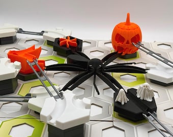 Puede incluir: Un juego de mesa con una base de cuadrícula hexagonal con baldosas blancas y verdes. El juego incluye una araña negra, una calabaza naranja, dos figuras de fantasmas blancos, una pieza de embudo naranja y conectores de pista grises.
