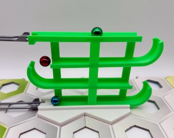 Pode incluir: Um componente de pista de berlindes em plástico verde brilhante com três níveis horizontais e extremidades curvas. Três esferas metálicas em vermelho, verde e azul estão posicionadas nas pistas. A estrutura liga-se a carris de metal cinzento.