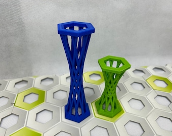 Puede incluir: Dos torres decorativas impresas en 3D, una azul y otra verde. Ambas tienen una parte superior hexagonal y un diseño similar a una celosía. Las torres están sobre una superficie con un patrón hexagonal.
