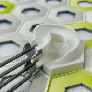 Op de afbeelding: Een wit plastic baanstuk met een gebogen helling en een grijs metalen baanstuk met twee rails. De baanstukken liggen op een groene en grijze zeshoekige tegel.