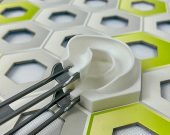 Pode incluir: Uma peça de pista de plástico branco com uma rampa curva e uma peça de pista de metal cinza com dois trilhos. As peças de pista estão sobre um azulejo hexagonal verde e cinza.