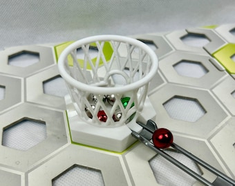 Puede incluir: Un aro de baloncesto de plástico blanco con una base de metal plateado y una canica roja, verde y plateada en su interior. El aro está unido a una pista de metal plateado.