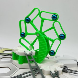 Peut inclure: Un jouet en plastique vert avec une roue tournante et des billes bleues. La roue a une base blanche et est attachée à une piste.