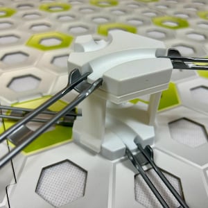 Puede incluir: Un componente blanco de pl&aacute;stico para circuito de canicas con pistas curvas y soportes met&aacute;licos. El componente est&aacute; sobre una base de baldosas hexagonales con detalles blancos, grises y verdes. Un juguete divertido y atractivo para ni&ntilde;os.
