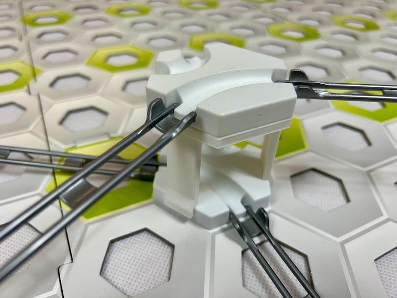 Puede incluir: Un componente blanco de pl&aacute;stico para circuito de canicas con pistas curvas y soportes met&aacute;licos. El componente est&aacute; sobre una base de baldosas hexagonales con detalles blancos, grises y verdes. Un juguete divertido y atractivo para ni&ntilde;os.