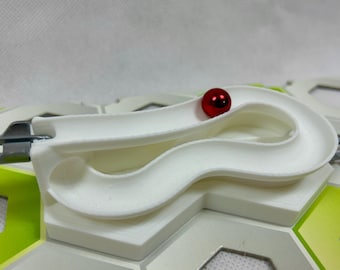 Pode incluir: Uma pista de mármore de plástico branco com uma bola de gude vermelha rolando por ela. A pista é projetada para ser usada com outras peças para criar uma pista de mármore personalizada.