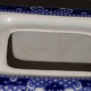 Puede incluir: Primer plano de un plato de porcelana blanco y azul con una abertura rectangular. El plato tiene un detallado patr&oacute;n floral azul alrededor de los bordes. El interior es blanco con algo de decoloraci&oacute;n.