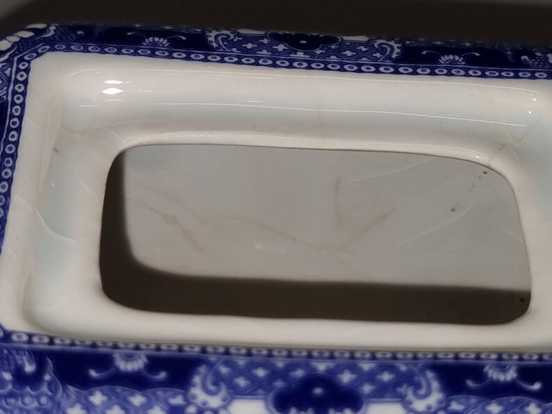 Puede incluir: Primer plano de un plato de porcelana blanco y azul con una abertura rectangular. El plato tiene un detallado patr&oacute;n floral azul alrededor de los bordes. El interior es blanco con algo de decoloraci&oacute;n.