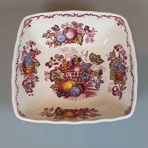 Puede incluir: Un cuenco cuadrado de cerámica con base de color crema y borde festoneado. El interior presenta un patrón de transferencia en tonos granate de cestas de frutas, uvas y hojas, con toques de azul, amarillo y verde en todo el diseño.