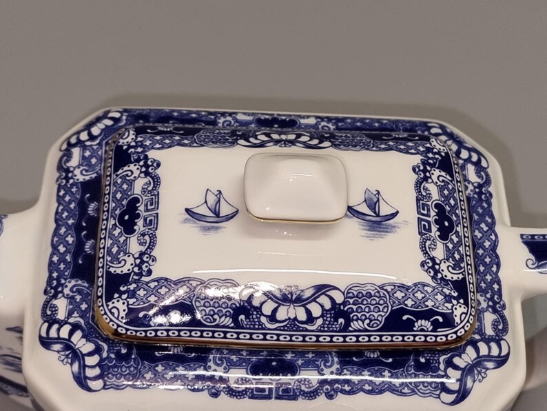 Puede incluir: Tapa de fuente de cer&aacute;mica blanca y azul con ribete dorado. La tapa presenta un dise&ntilde;o de velero azul y blanco y patrones decorativos. El asa es un peque&ntilde;o cuadrado blanco con ribete dorado.
