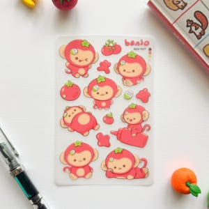 May include: A clear sticker sheet featuring multiple cartoon monkeys dressed in red tomato-themed costumes. The sheet includes the text "banjo" and "peko puff" in red letters, along with various tomato illustrations and small red shapes.