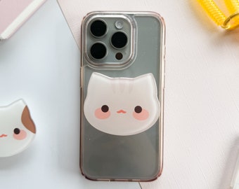 May include: A clear phone case with a gray background and a white cat face pop socket. The cat face has pink cheeks and a small pink nose.